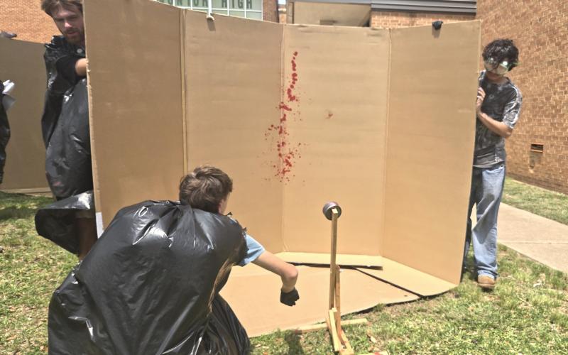Students hold up a card board box as another student uses a tool to create a blood spatter pattern. The pattern was created by one of many investigative student teams in the forensic science class at Breckenridge High School. (BISD Journalism/Contributed photo)