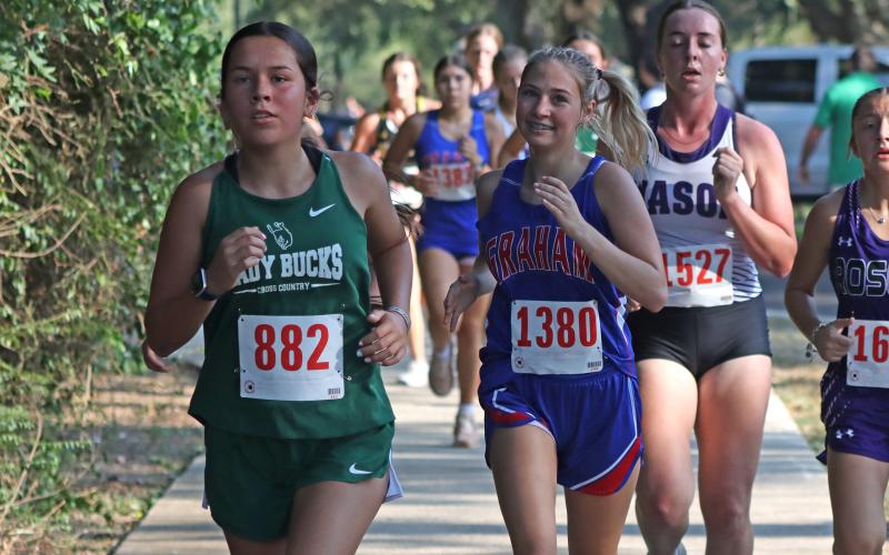 (Photo/Liam Bailey) A Lady Bucks cross country runner runs in front of a Graham runner during the Brownwood Invitational that took place Wednesday, Aug. 27. 