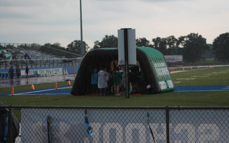 Buckaroo helpers huddle under the entrance tunnel prior to the game starting. Rain poured before and during the game, causing viewers to huddle under umbrellas or other structures to avoid the rain. BA photo by James Norman